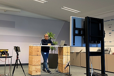 Mann am Schreibtisch nimmt über einen großen Bildschirm an einer Online-Konferenz teil ©Frauscher